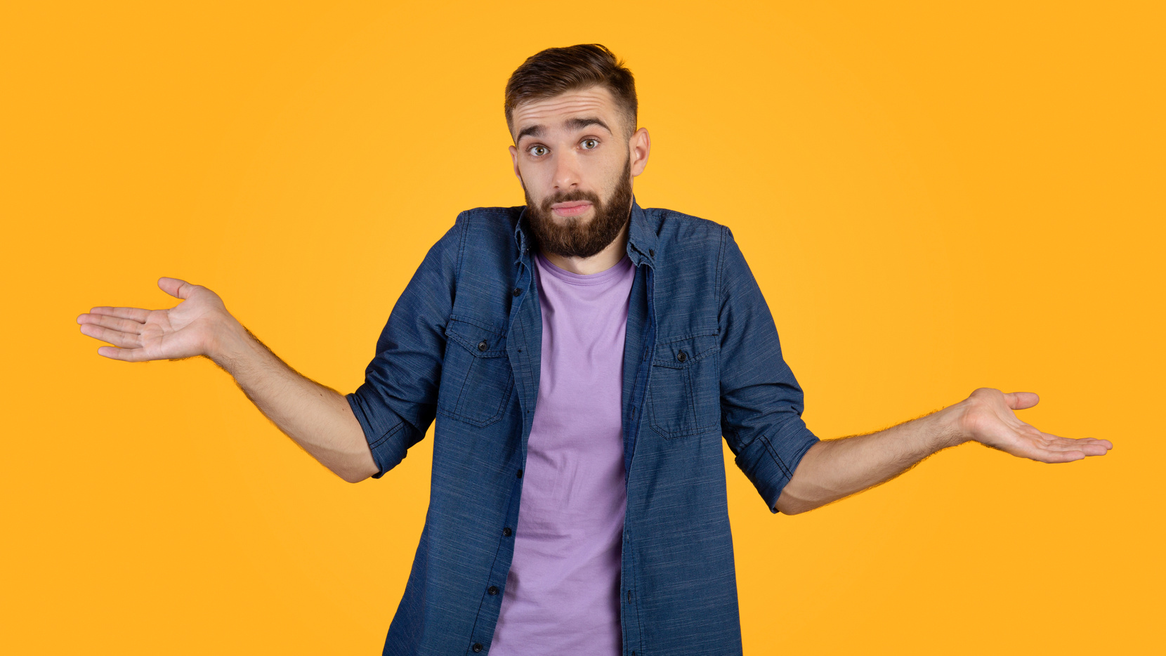 I don't know. Handsome Caucasian guy shrugging shoulders, feeling puzzled or uncertain on orange studio background